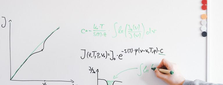 Whiteboard mit einem gezeichnet Diagramm. Daneben wurden zwei Formeln geschrieben. Darunter hält eine Hand einen Stift und zeichnet ein Diagramm.